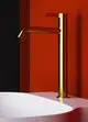 Standventil in gebürstetem Gold mit langer Ausladung, montiert nahe einer weißen Wanne in einem Raum mit roten und schwarzen Wänden, gefertigt von Ideal Standard.